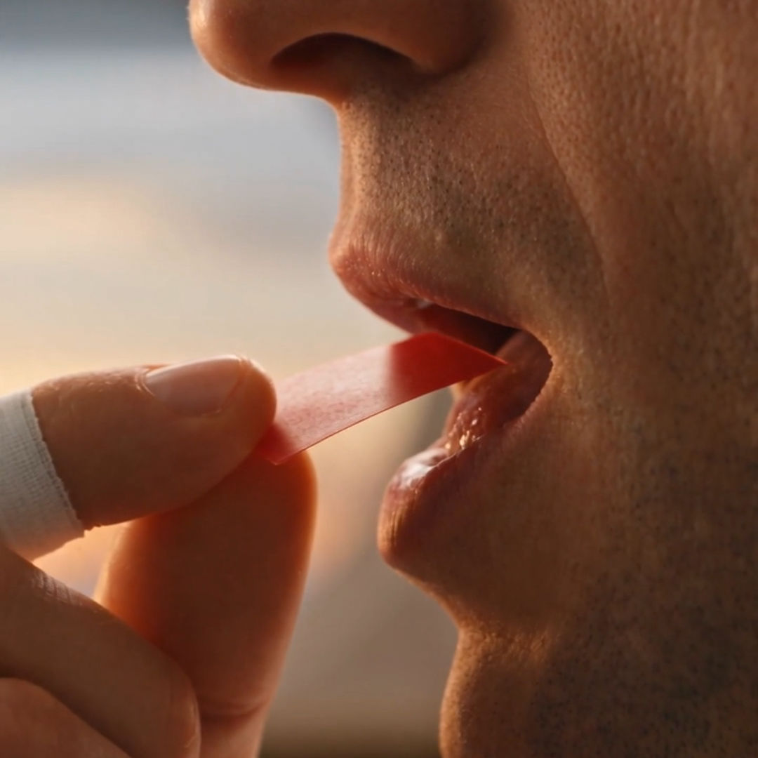 Macro close-up of an athlete placing a paper-thin translucent cranberry NRGStrip on the tongue